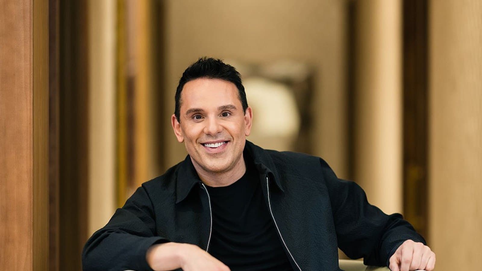 An investor seated in an armchair in a hotel corridor, smiling towards the camera. File photograph. Foto d'archivio.