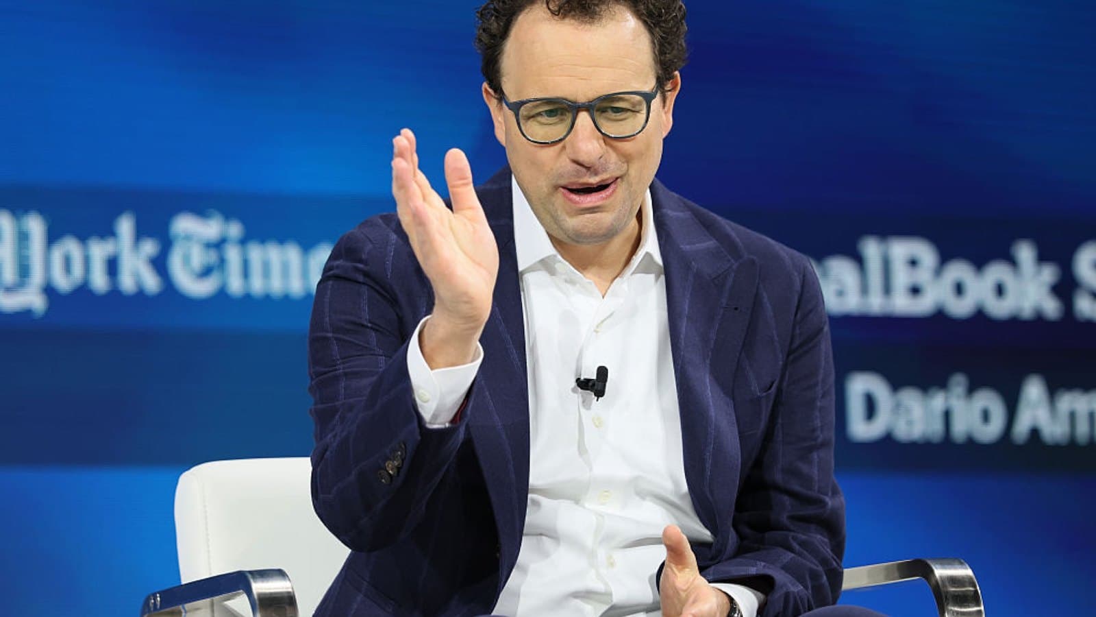 Dario Amodei speaking on stage at a conference, gesturing with one hand in front of a blue backdrop. Foto d'archivio.