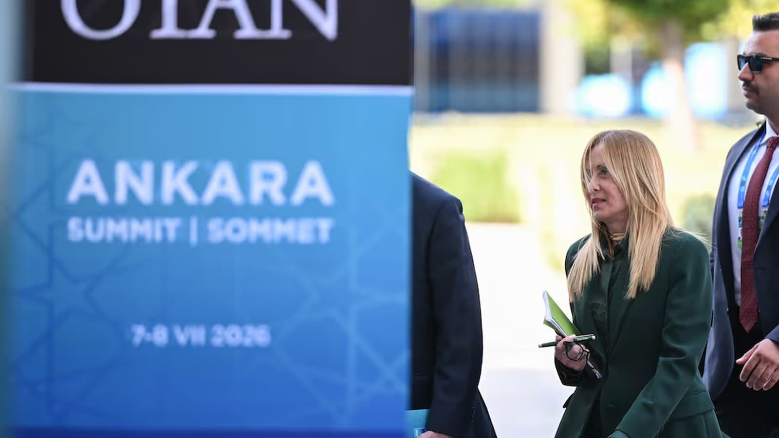 Giorgia Meloni cammina davanti al cartello del vertice NATO di Ankara, affiancata dalla sicurezza.