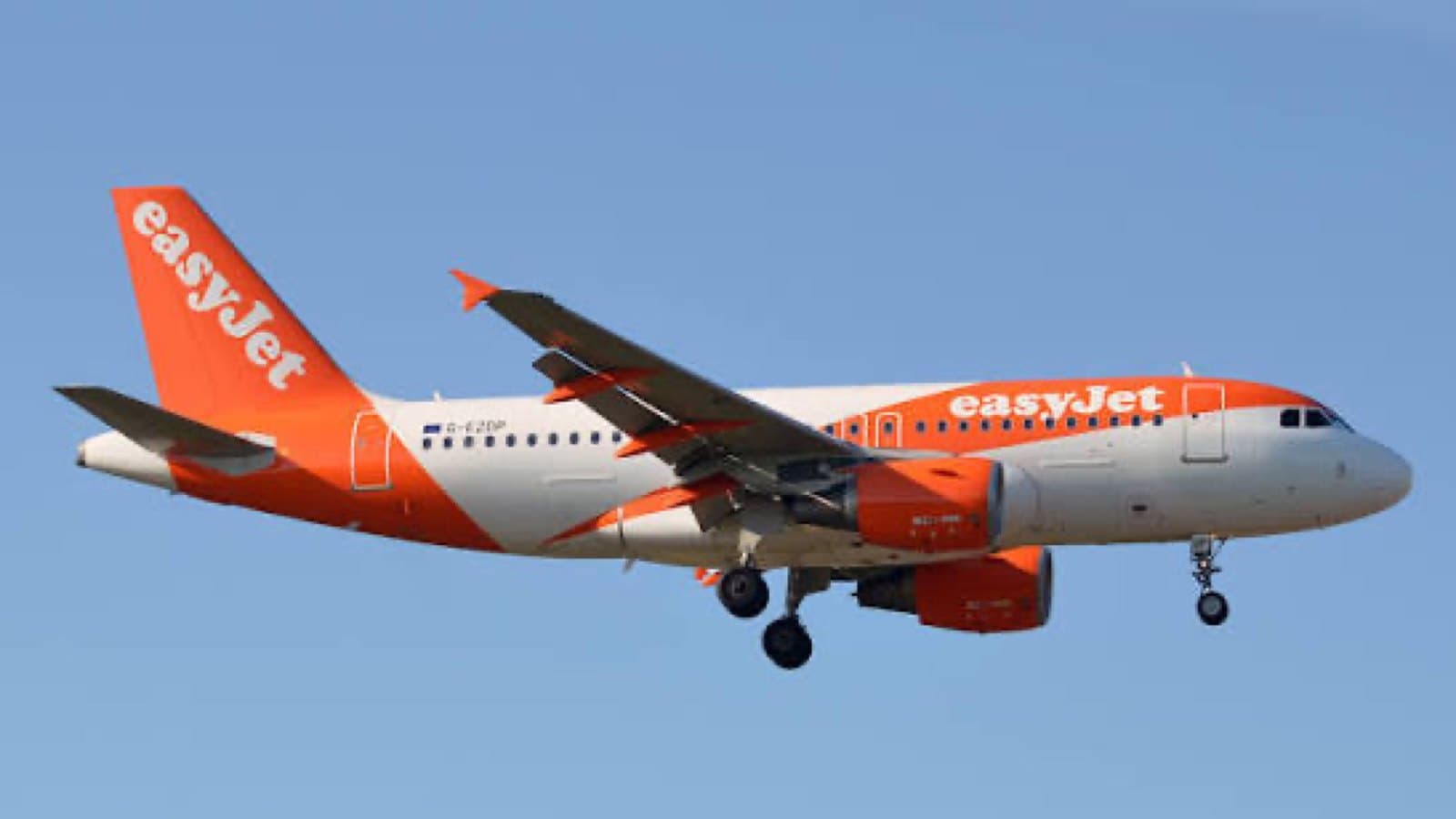 An easyJet Airbus A319 in orange and white livery on approach with its landing gear down against a clear sky. Foto d'archivio.