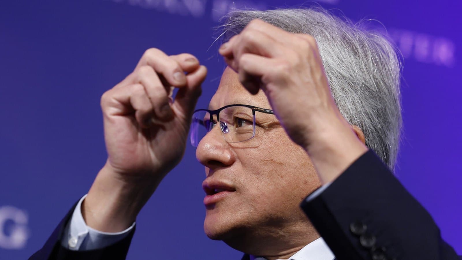 Jensen Huang gesturing with both hands while speaking on stage against a purple backdrop. Foto d'archivio.