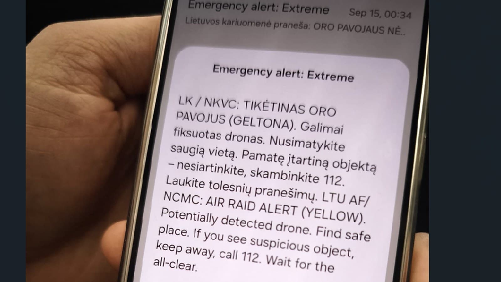 A hand holds a phone displaying an extreme emergency alert about a possible drone in Lithuanian airspace.