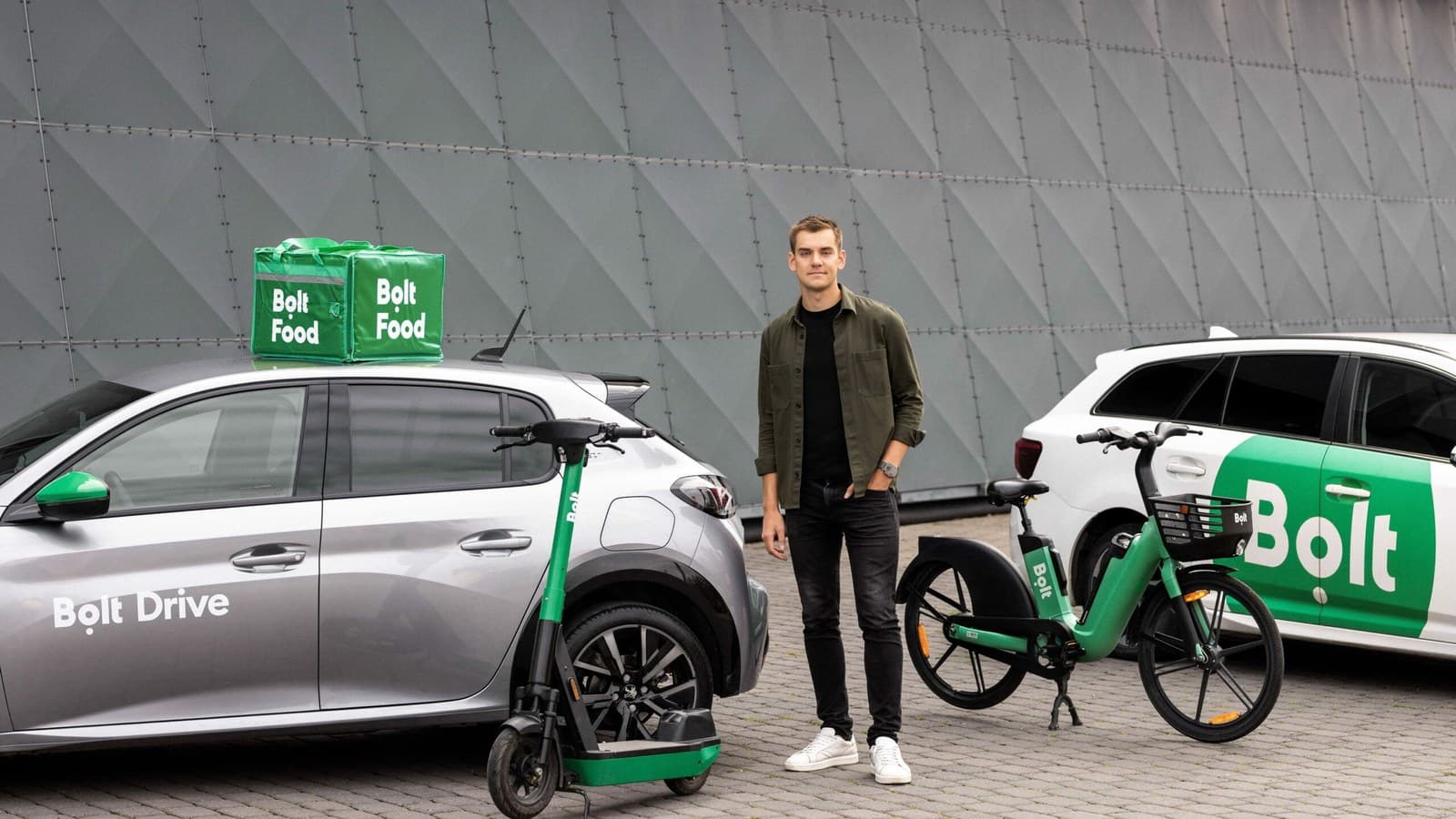 Markus Villig in piedi tra un'auto Bolt Drive e un monopattino e una bici Bolt, con una camicia verde.