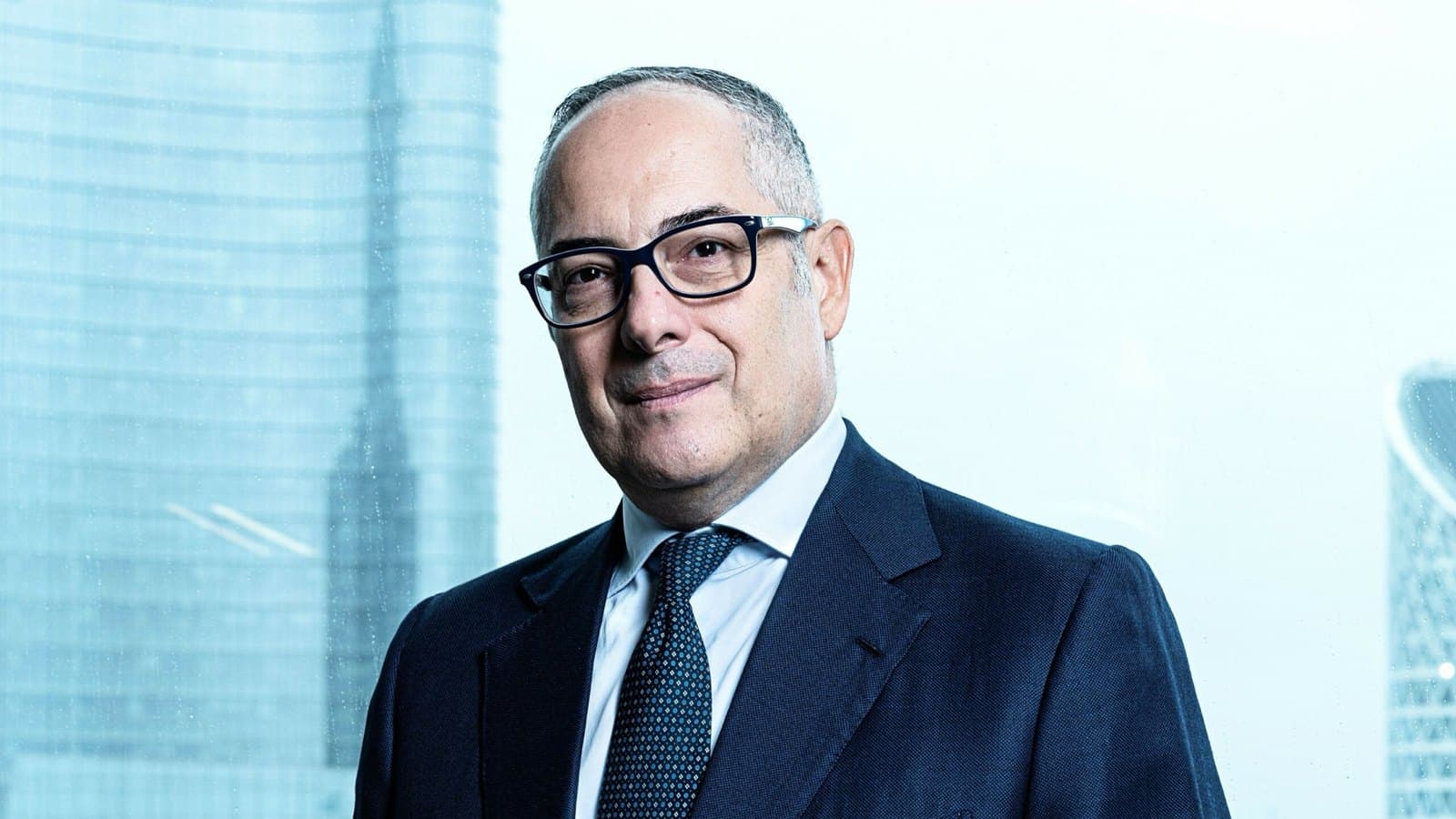 Mauro Macchi, chief executive of Accenture Emea, in a dark suit and glasses, photographed against a window overlooking the Milan skyline. Foto d'archivio.