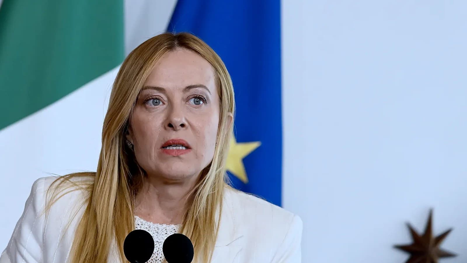 Giorgia Meloni parla da un podio davanti alle bandiere italiana ed europea.
