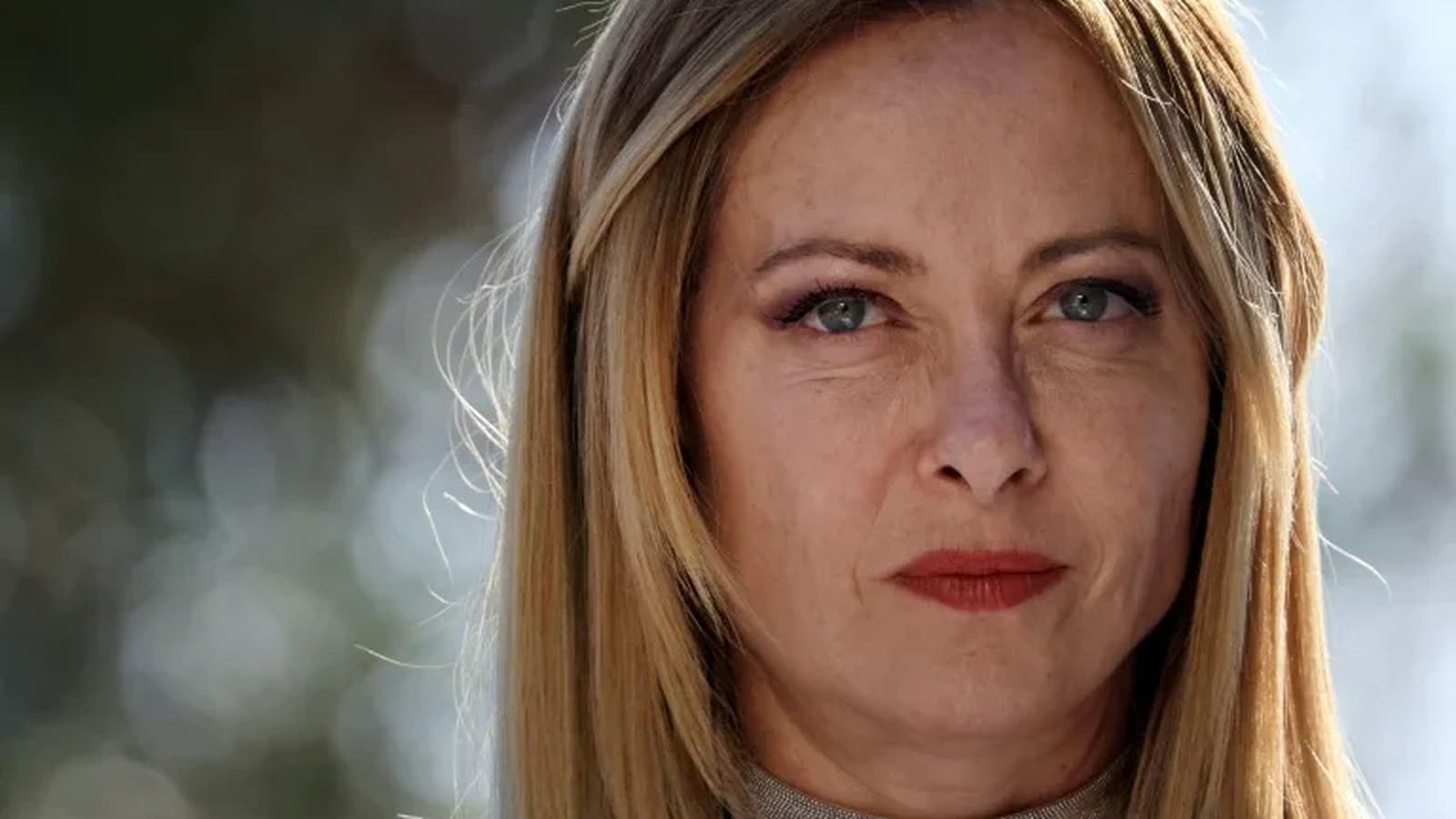 Giorgia Meloni guarda dritto verso l'obiettivo in un primo piano all'aperto.