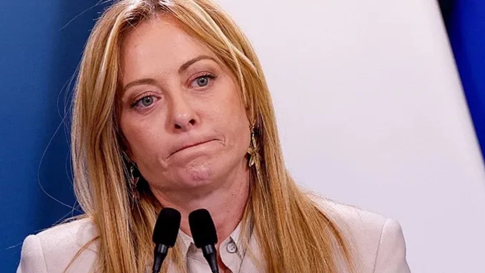 Giorgia Meloni grimaces while speaking at microphones during a press event.