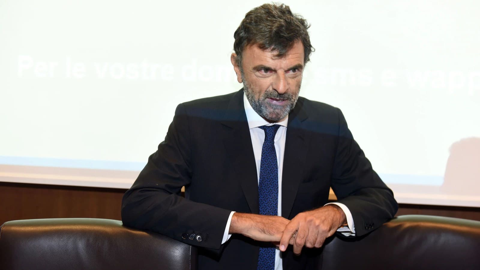 Paolo Molesini, president of Assoreti, leans on a chair back while speaking at a conference.