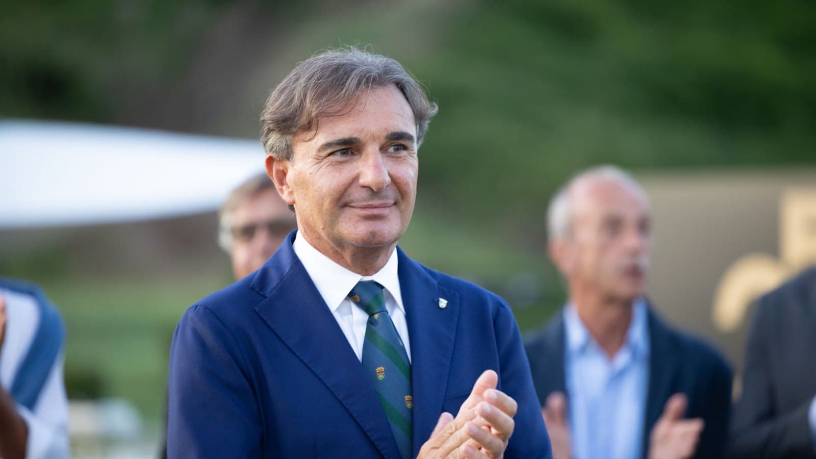 Pietro Gasbarra, president of the Golf Club Parco di Roma, applauding in a blue blazer and club tie outdoors. Foto d'archivio.
