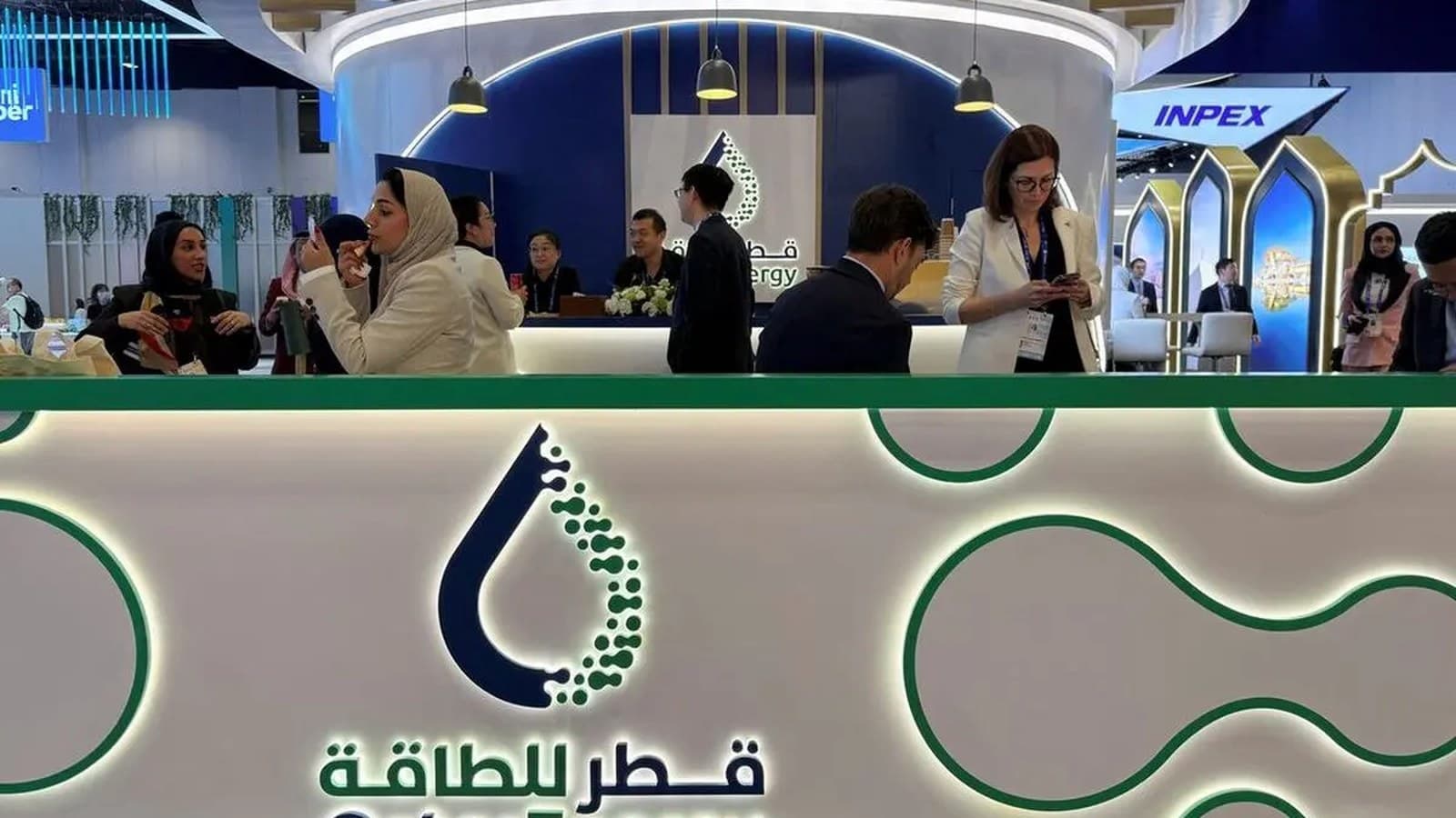 People gather at the QatarEnergy booth beneath its logo at an industry conference.