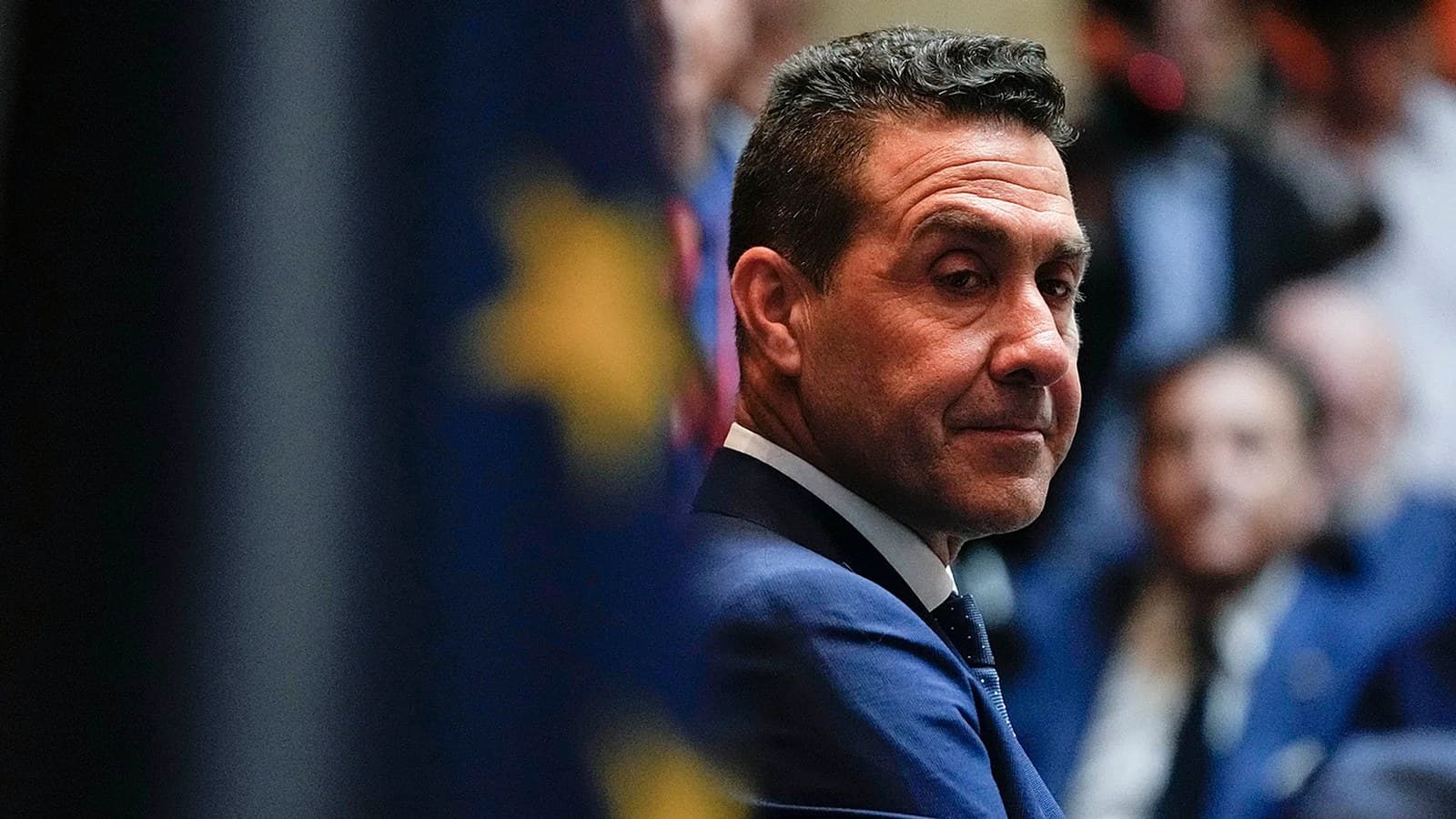 Roberto Vannacci guarda alle sue spalle in giacca e cravatta, con una bandiera dell'Unione europea visibile sullo sfondo.