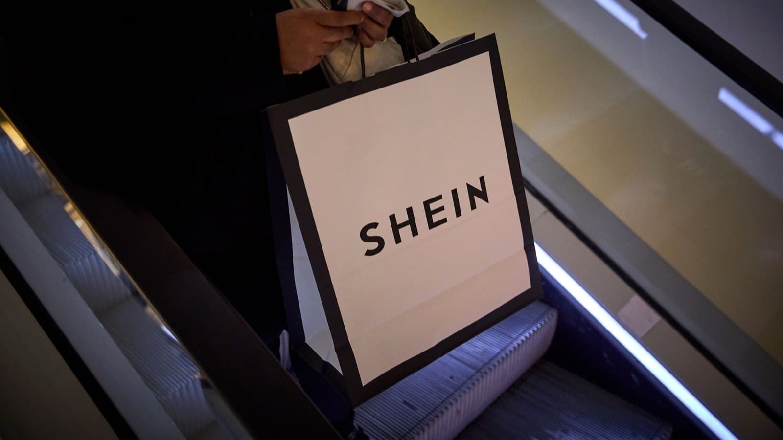 A shopper on an escalator carrying a paper bag printed with the Shein logo. Foto d'archivio.