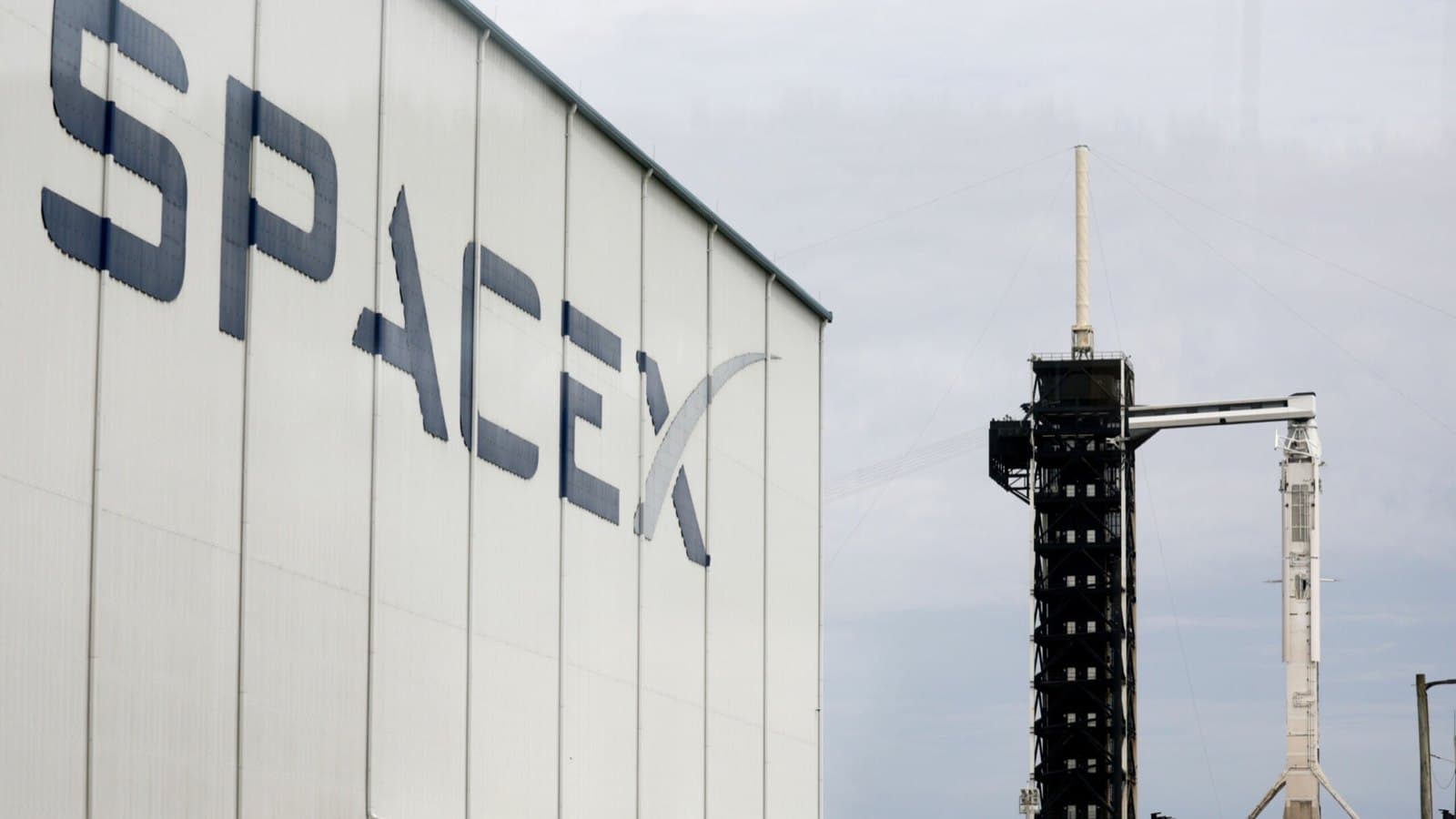 The SpaceX logo on the side of a hangar at Cape Canaveral, with a rocket standing on the launch pad beyond it. Foto d'archivio.