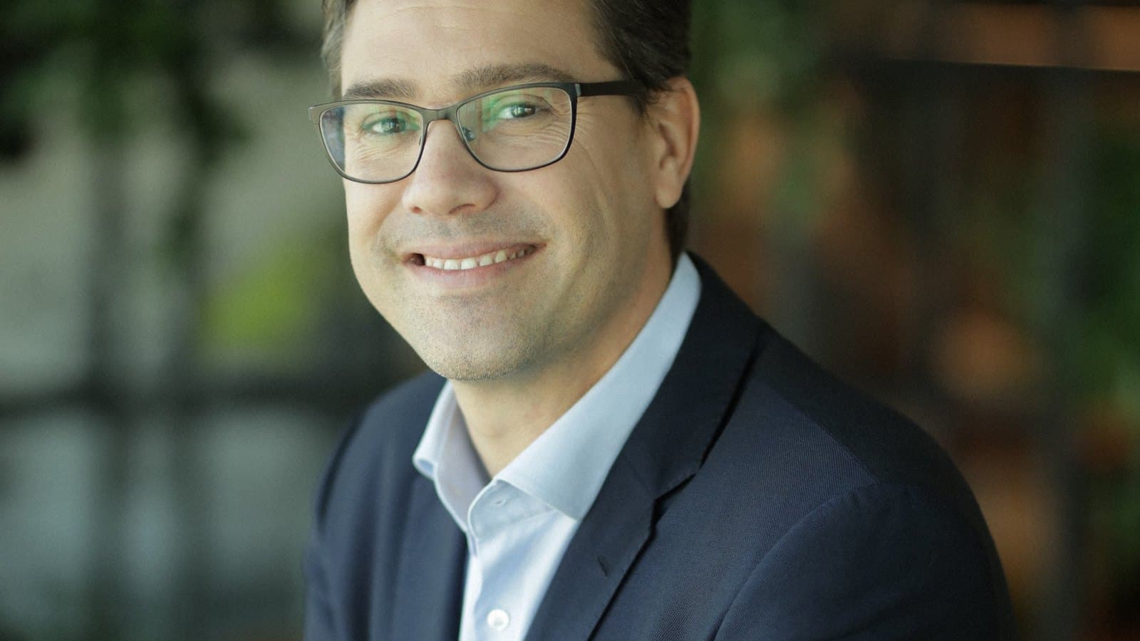 Yoni Assia, co-founder and chief executive of eToro, in a navy jacket and glasses against a blurred green background. Foto d'archivio.