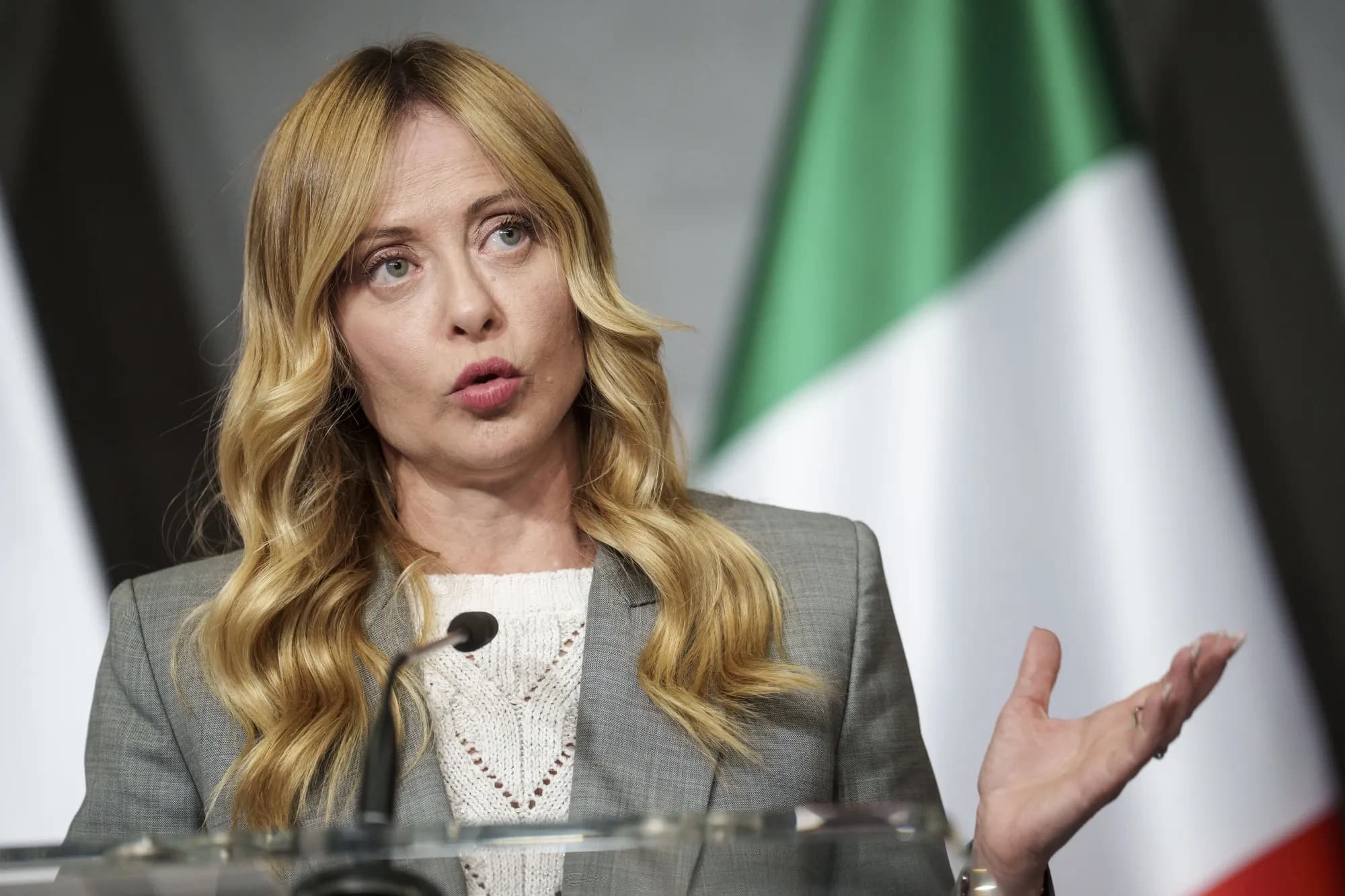 Giorgia Meloni parla a un podio davanti alla bandiera italiana.