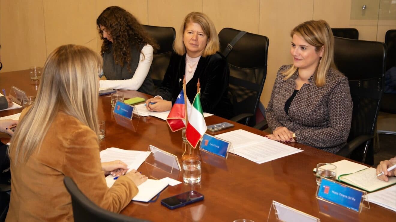 Funzionari italiani e cileni, tra cui Maria Tripodi e Maria Teresa del Re, riuniti attorno a un tavolo a Santiago con le bandiere di Italia e Cile.
