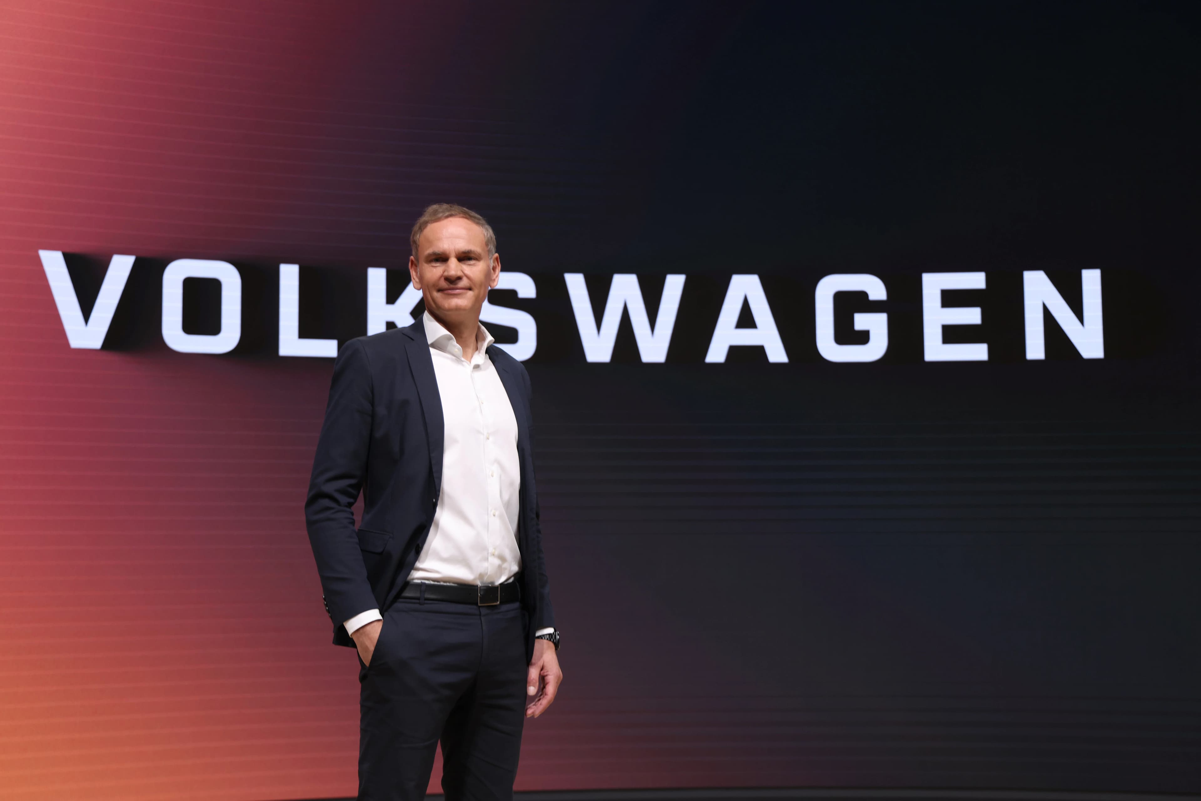 L'amministratore delegato di Volkswagen Oliver Blume davanti al logo Volkswagen illuminato sul palco.